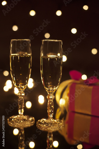 Pair bocal filled champagne with reflection on the glass. In the background, a gift in blurring