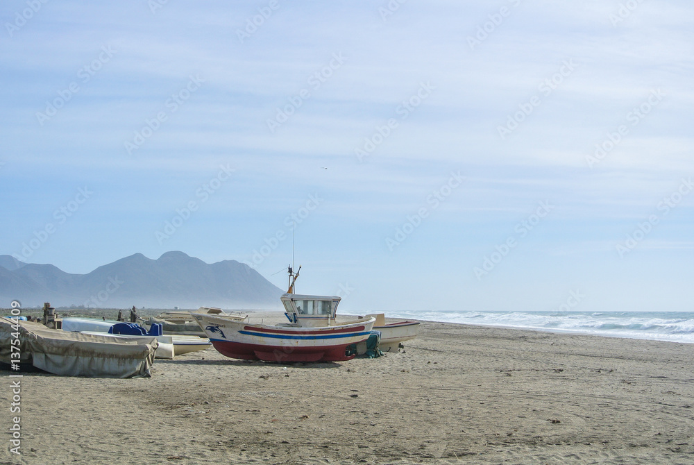Cloudy day at the lonely beach with colored boats on the shore not far from mountains.