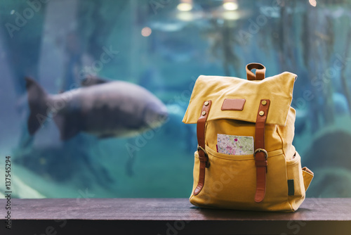 Hipster yellow backpack and map closeup. View from front tourist traveler bag on background blue sea aquarium. Person hiker visiting oceanarium museum in Barcelona on backdrop, blank blurred mockup