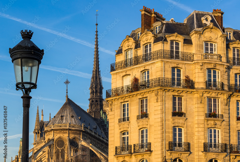 Haussmannian building facade on Ile de la Cite with Notre Dame Cathedral Spire and street lamp post. 4th Arrondissement, Paris, France