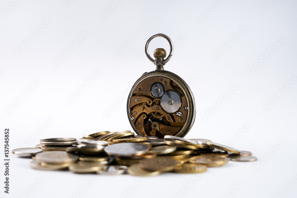 Old Clockwork with open cover on scattered coins isolated on white.Time is money concept. Old Clockwork with open cover on scattered coins isolated on white.Time is money concept.