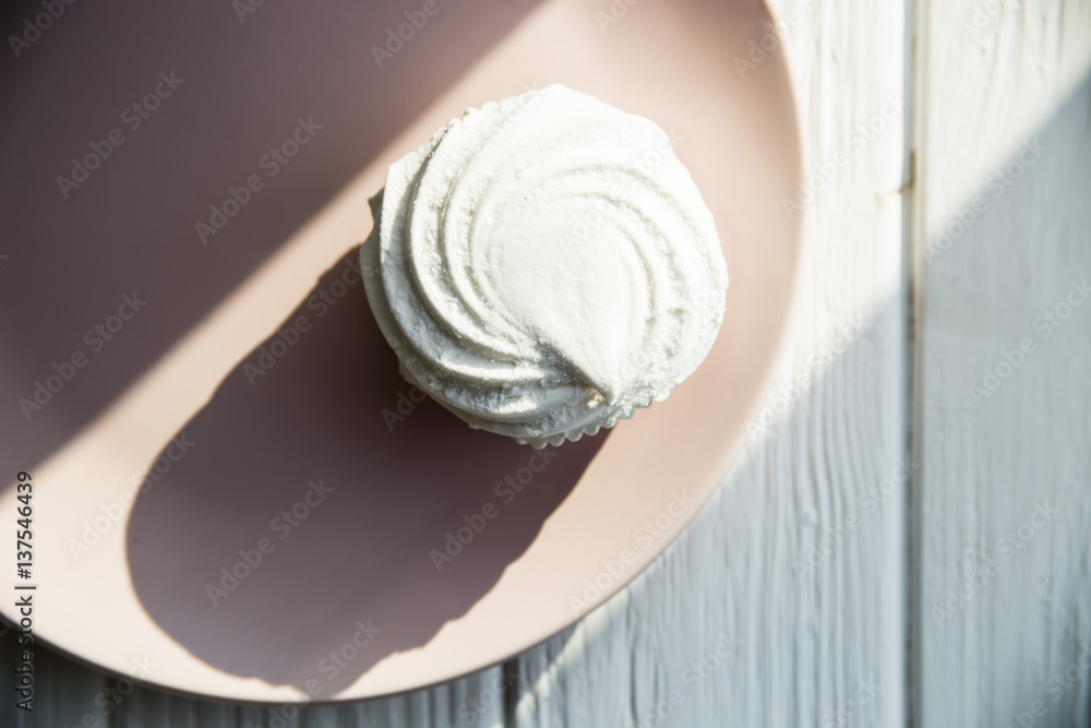 Fototapeta premium White sweet marshmallow air and gentle pink round dish on a white wooden table