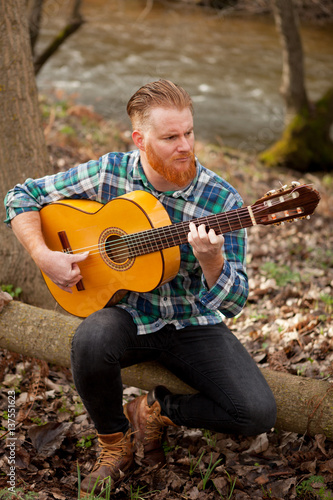 Hipster man with red beard with a guitar in the field