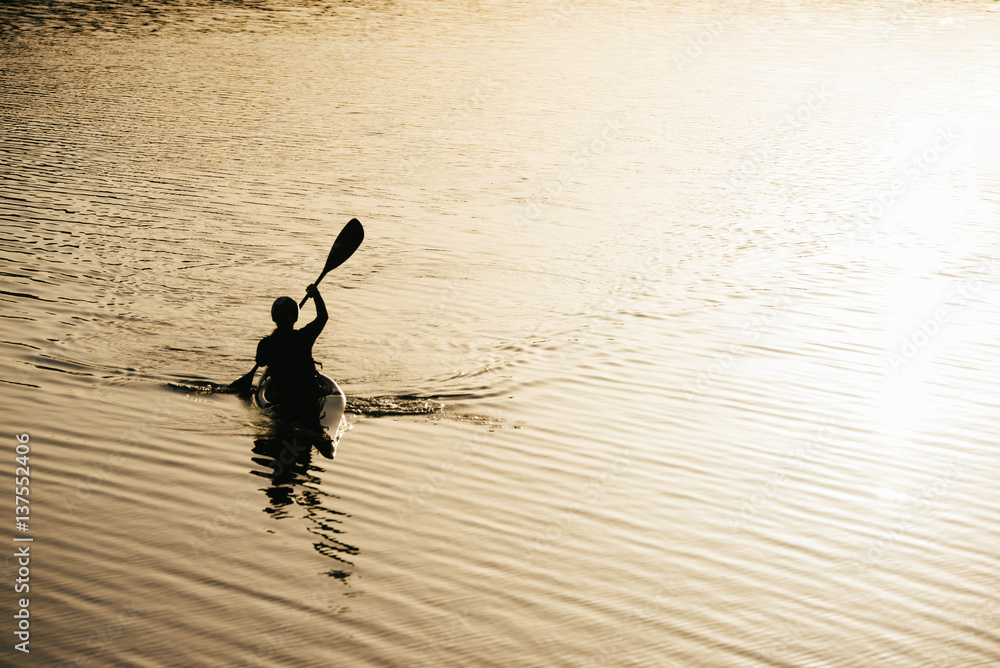 Young female canoer paddling on the lake in the morning.