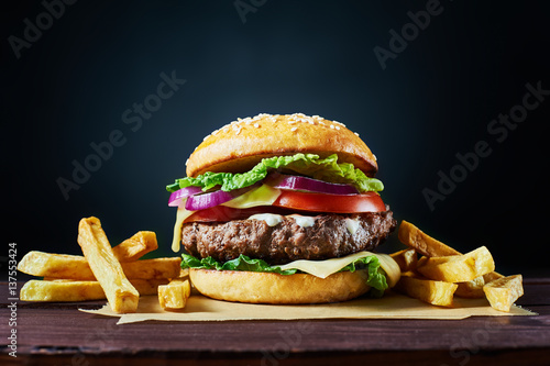 Tableau sur toile Burger de boeuf artisanal et frites français sur une table en bois isolée sur fond sombre