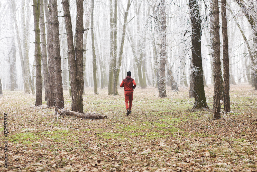 Back view of young sportsman running in misty winter forest. Back view of young sportsman running in misty winter forest.