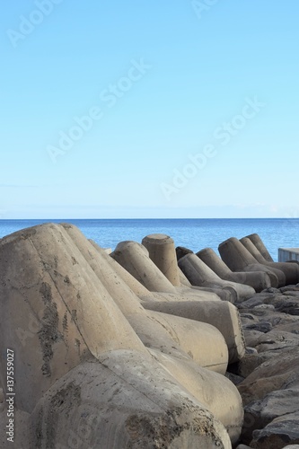 Mächtige Tetrapoden am Ufer zur Befestigung und zum Schutz der Küste, im Hintergrund das Meer, vor tiefblauem Himmel