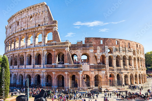 Fototapet Ruins of the colosseum in Rome, walking visitors and tourists, sunny day with bl