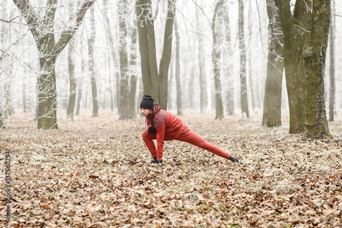 Young male jogger stretching arms muscles and warming up before running outdoors in winter.