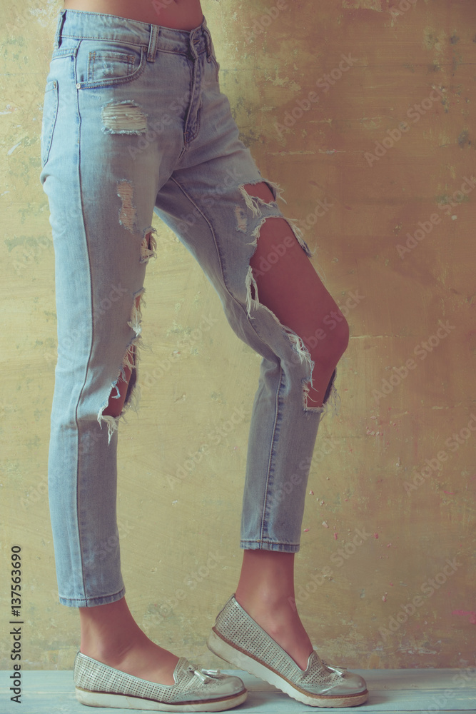 Ripped jeans female feet. Gorgeous girl in torn jeans over studio  background. Lady in fashionable ripped jeans stands in gray wall. Sexy  young woman in trendy clothes on a grunge background Stock