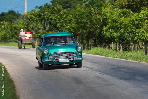 Grüner Oldtimer fährt auf der Landstrasse von Santa Clara in Kuba mit Pferdekutsche im Hintergrund - Serie Kuba Reportage