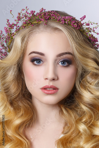 Beauty portrait of a blonde girl with chic curls in a wreath of heather isolated on a gray background.