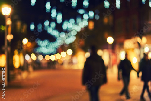Blurred city street with their Christmas decorations. Trees decorated with bright garlands. People walking holidays. Bokeh basic background for design