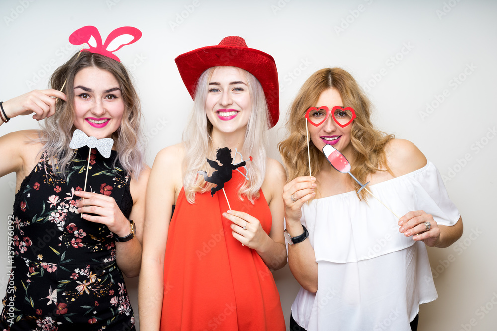 three happy young ladies girls strike a pose on white background photo booth with party props