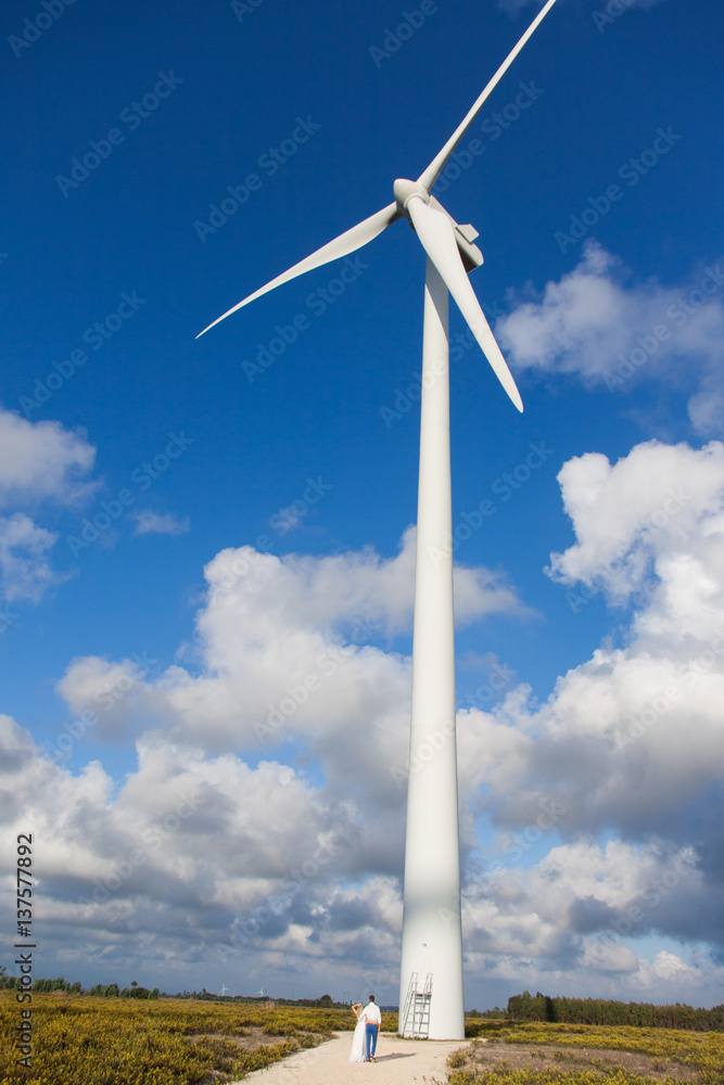 A young couple from near wind generators in field on a background beautiful clouds A young couple from near wind generators in field on a background beautiful clouds