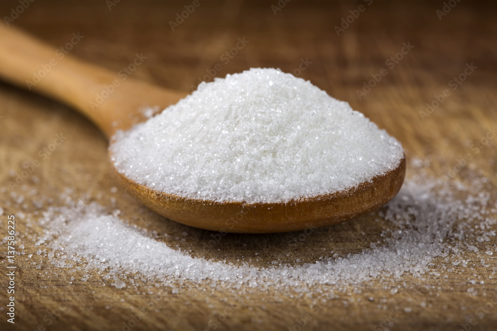 Close up of one bamboo spoon filled with white sugar on wood Close up of one bamboo spoon filled with white sugar on wood