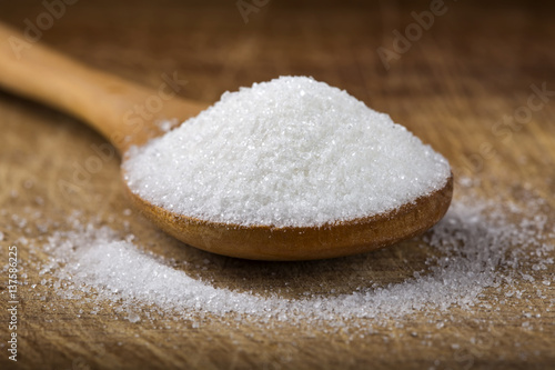 Close up of one bamboo spoon filled with white sugar on wood