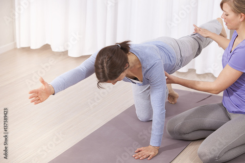 Fitness instructor supports woman on Pilates class