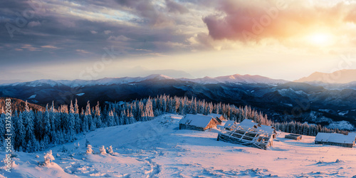 Fantastic sunset over snow-capped mountains and wooden chalets. 