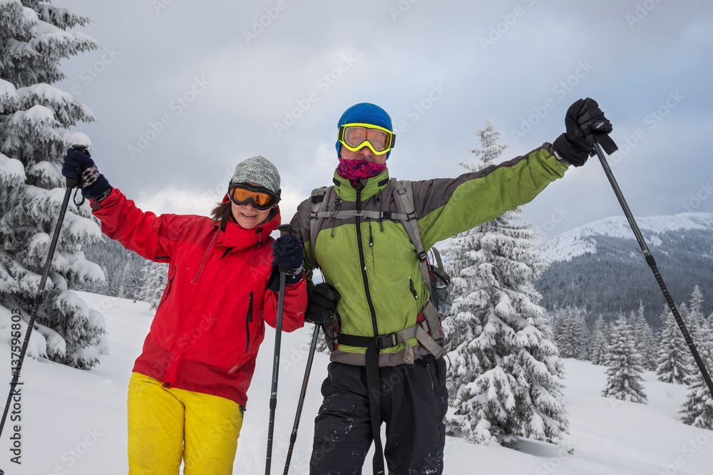 Couple of joyful travelers in goggles stands at alpine meadow