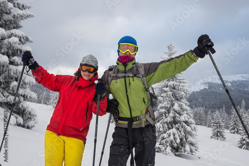 Couple of joyful travelers in goggles stands at alpine meadow