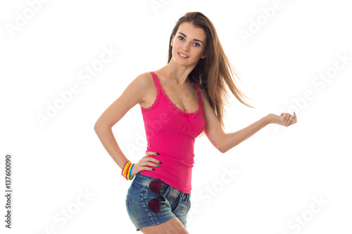 Charming young brunette woman in pink shirt and jeans shorts posing on camera isolated on white background