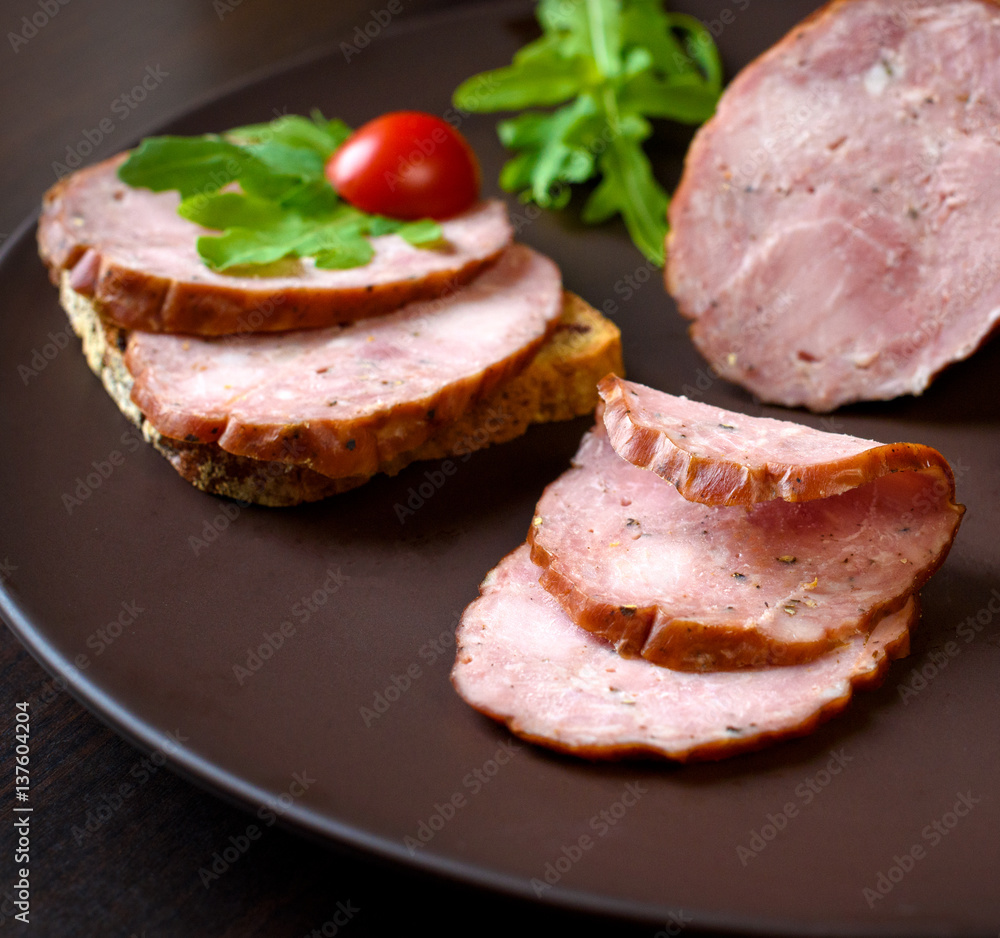 Smoked sausage, ham with red tomatoes and lamb's lettuce on a dark brown plate Smoked sausage, ham with red tomatoes and lamb's lettuce on a dark brown plate