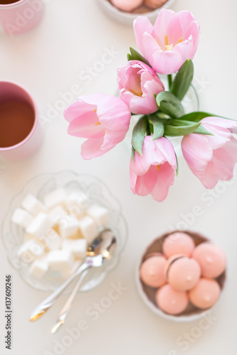 Spring background. Sweets and tea on a table with pink tulips. Still life with fresh bouquet of tulips. Beautifully decorated tray.