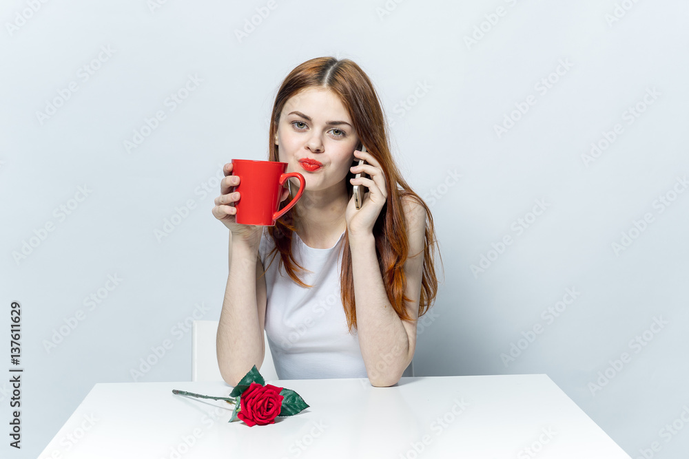 a woman is sitting at a table and holding a red cup in her hand, a flower