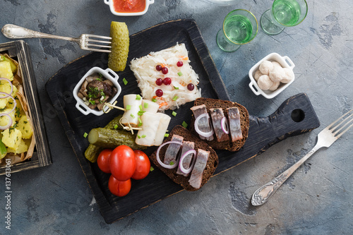 Appetizer food, herring and rye bread on wooden board with vodka and pickles