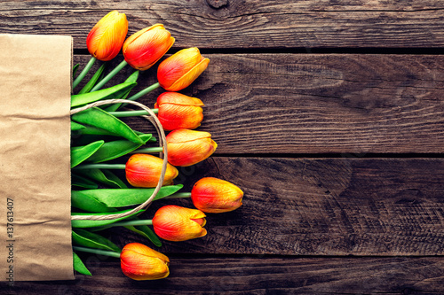 Fototapeta Naklejka Na Ścianę i Meble -  Bouquet of tulips in a paper shopping bag on a wooden background, concept of discounts and sales on the Women's Day or Mother's Day or Easter