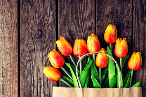 Fototapeta Naklejka Na Ścianę i Meble -  Bouquet of tulips in a paper shopping bag on a wooden background, concept of discounts and sales on the Women's Day or Mother's Day or Easter