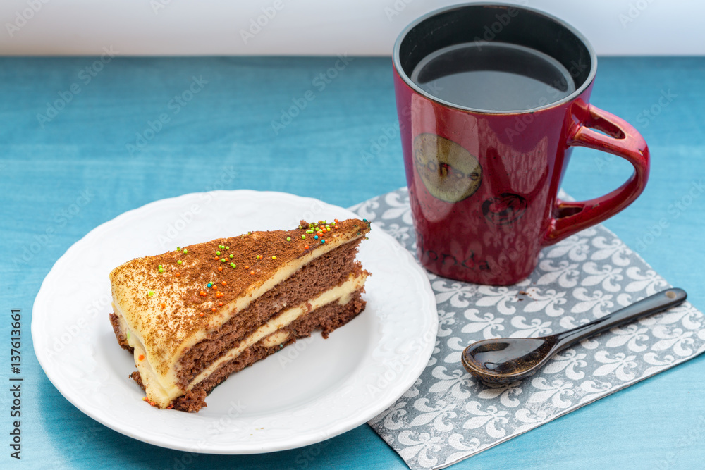 Cake piece with coffee in red cup on turquoise table Cake piece with coffee in red cup on turquoise table