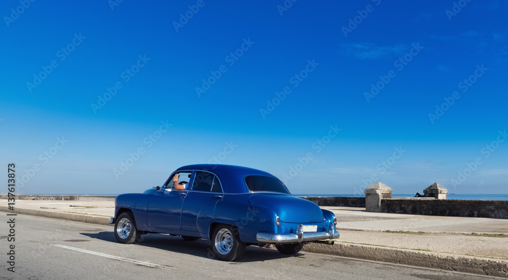 Blauer amerikanischer Oldtimer fährt auf dem Malecon im Hintergrund die karibische See in Havanna Kuba - Serie Kuba Reportage