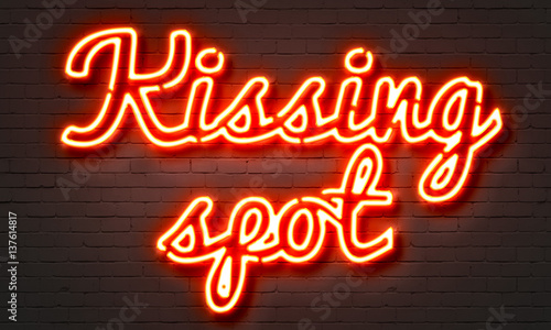 Kissing spot neon sign on brick wall background.