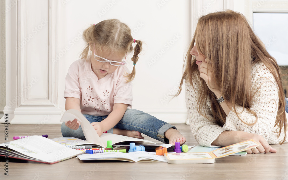 The daughter and mother sit on the floor and draw. The woman helps to the child to draw with markers. The daughter and mother sit on the floor and draw. The woman helps to the child to draw with markers.