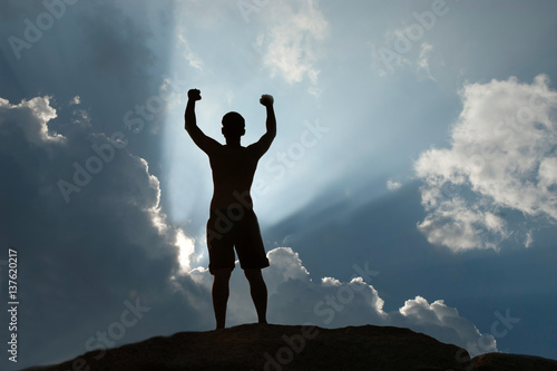 Positive male holding hand up and expressing gladness while standing on stone.