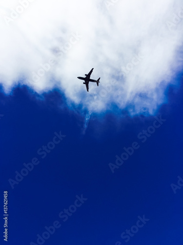 Photography Silhouette of a plane against white clouds and a blue sky.