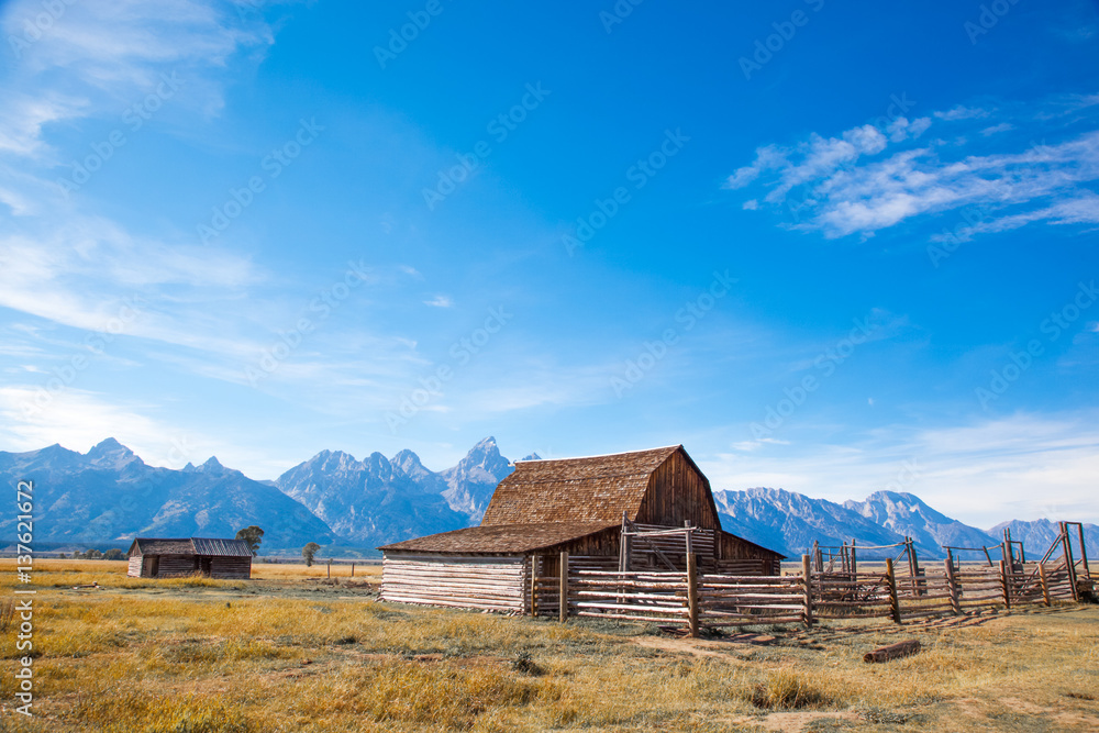 Grand Teton National Park, Jackson Hole, Wyoming. Barn in a grass field plain against the Grand Teton mountain range with the sun shining Grand Teton National Park, Jackson Hole, Wyoming. Barn in a grass field plain against the Grand Teton mountain range with the sun shining