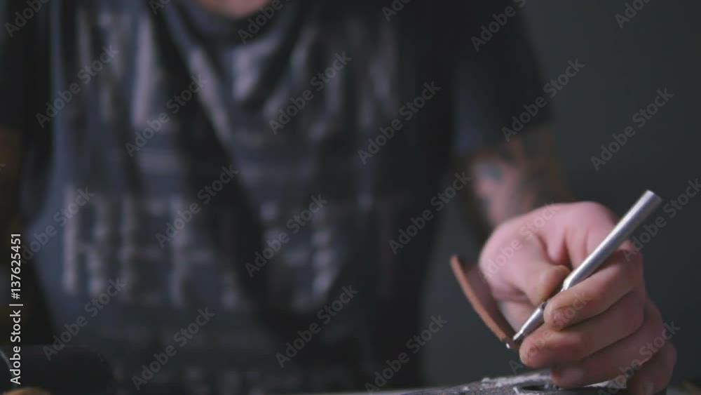 Closeup view of man's hands making holes in a leather strip in the workshop, slow motion Closeup view of man's hands making holes in a leather strip in the workshop, slow motion