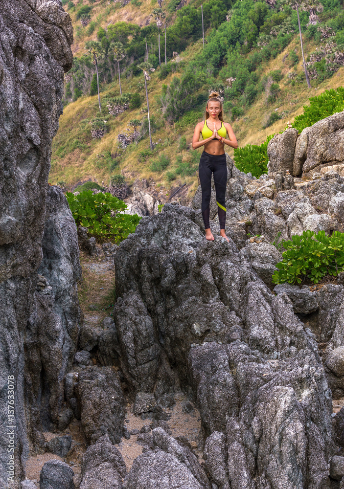 Woman doing yoga on a rock. Young woman standing at the edge of the cliff with praying hands. Vertical outdoors shot.