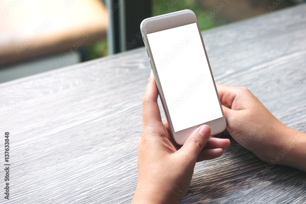 Mockup image of hands holding white mobile phone with blank white screen on vintage wooden table