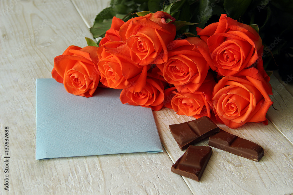 Bouquet of red roses with chocolate and blue envelope on a wooden background