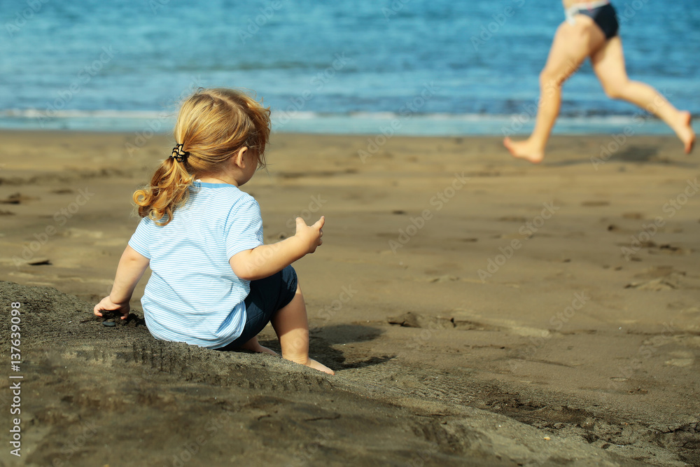 Cute baby boy sits on sand on sandy beach Cute baby boy sits on sand on sandy beach