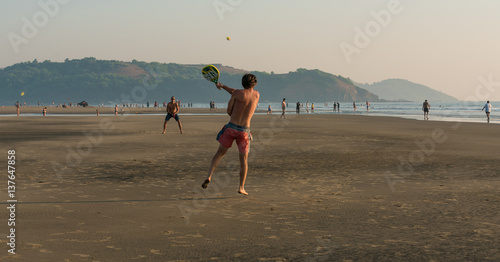 men play with a ball and rackets on the beach