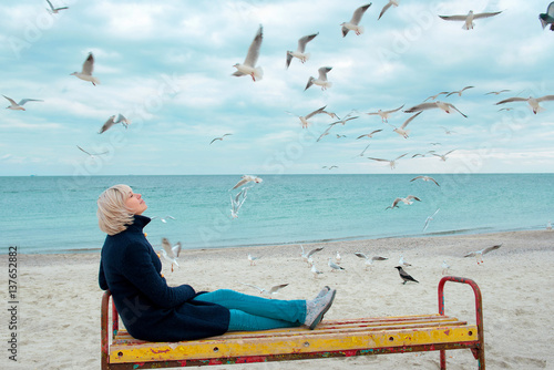 blonde woman and seagulls in cloudy autumn day on the sea coast 
