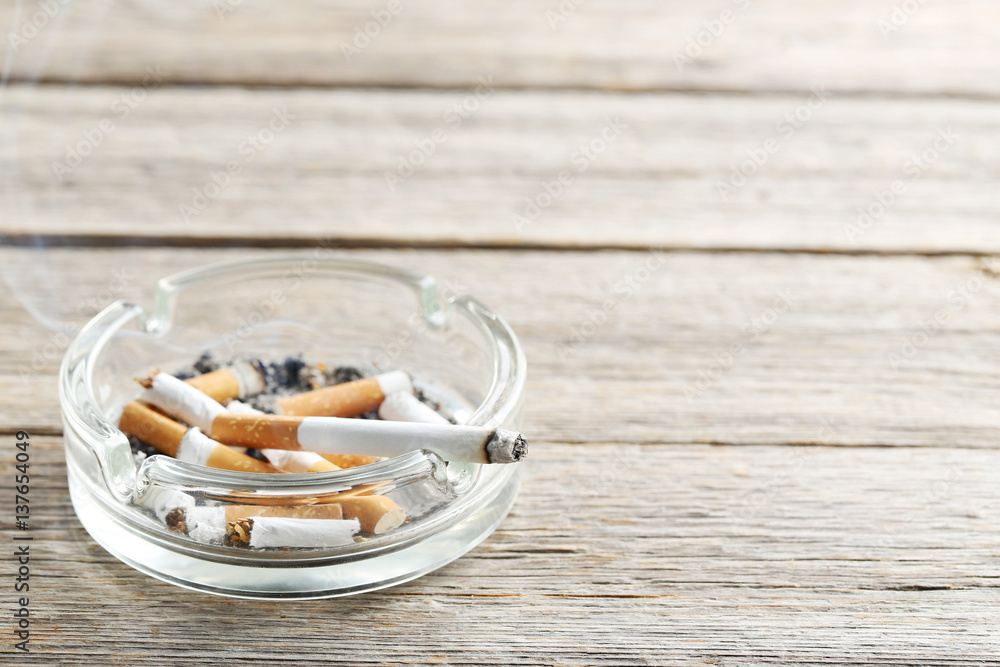 Cigarette butts with ash in ashtray on grey wooden table