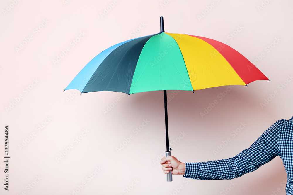 Colorful umbrella in male hand on beige background