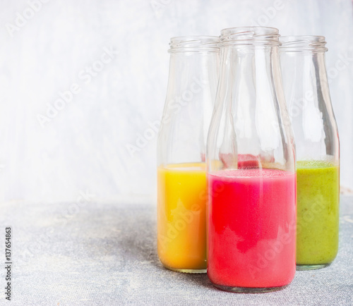 Bottles with colorful drinks: smoothies or juices on light background, front view
