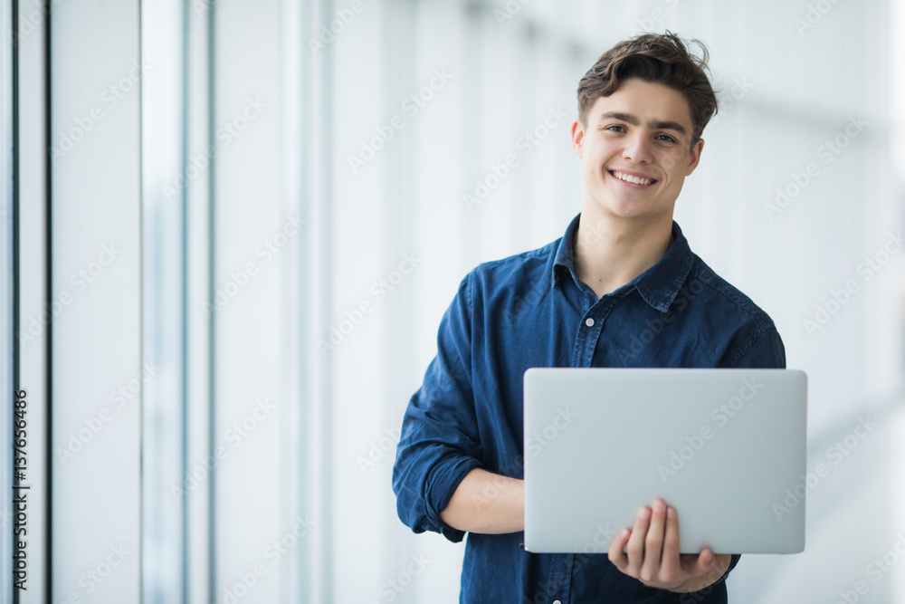 Fototapeta premium Handsome young man man holding a laptop in hall